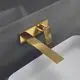 Wand-Waschtischarmatur mit eckiger Rosette in Brushed Gold, montiert an einer grauen Wand mit weißem Waschbecken. Produkt von Ideal Standard.